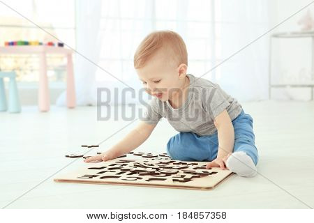 Cute little child playing with letters while sitting on floor at home