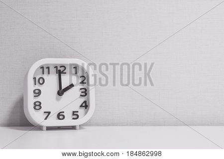 Closeup white clock for decorate in 2 o'clock on white wood desk and cream wallpaper textured background in black and white tone with copy space