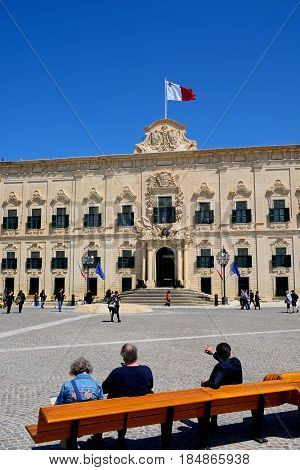 VALLETTA, MALTA - MARCH 30, 2017 - View of the Auberge de Castille (office of the Prime Minister) in Castille Square with tourists sitting on a bench in the foreground Valletta Malta Europe, March 30, 2017.
