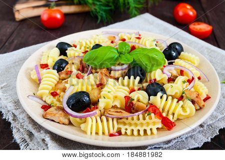 Pasta salad radiatori with chicken black olives blue onion sweet pepper on a dark wooden background.