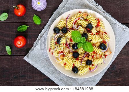 Pasta salad radiatori with chicken black olives blue onion sweet pepper on a dark wooden background. The top view.