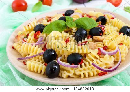 Pasta salad radiatori with chicken black olives blue onion sweet pepper on a white wooden background. Close up