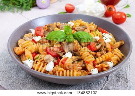 Pasta Radiatori with chicken mushrooms cherry tomatoes feta cheese and tomato sauce on a light background.