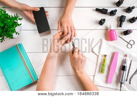 Manicure for the client. Close-up of the hands of a manicurist and client on a wooden background. Nail care. Manicure set and nail polish.
