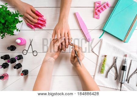 Manicure for the client. Close-up of the hands of a manicurist and client on a wooden background. Nail care. Manicure set and nail polish.