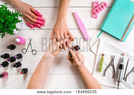 Manicure for the client. Close-up of the hands of a manicurist and client on a wooden background. Nail care. Manicure set and nail polish.
