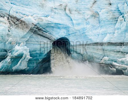 Large volume of melt water gushes from large hole in the face of glacier in the bay Tracy Arm Alaska.