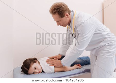 Lay here for a minute. Wise capable qualified rheumatologist explaining little girl she needing relaxation after he conducting medical massage