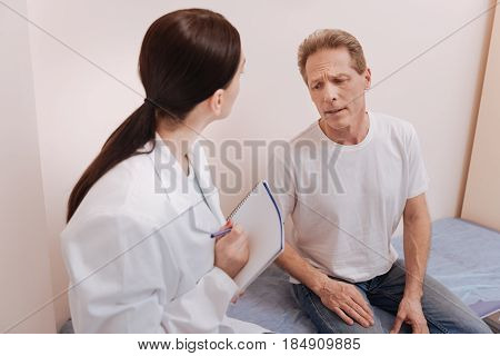 Pain is unbearable. Concerned hurt middle aged patient visiting his doctor and explaining what he feeling while having some troubles with his back