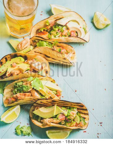 Healthy corn tortillas with grilled chicken, avocado, fresh salsa, limes and beer in glass over blue wooden background, selective focus, copy space. Gluten-free, allergy-friendly, dieting concept