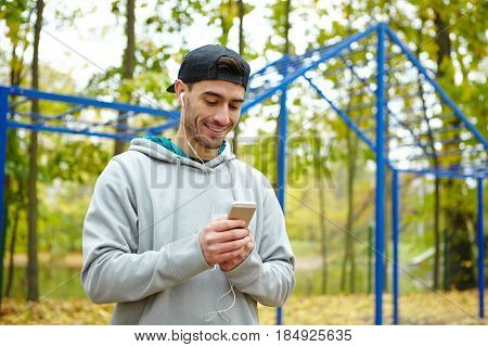 Waist-up portrait of joyful young sportsman listening to music on smartphone in order to psych himself up for effective workout