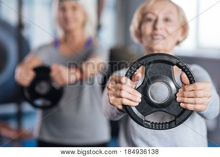 Physical activities. Selective focus of a weight disc being held by a nice active aged woman while doing physical activities