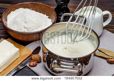 Preparation of bechamel sauce in a pan and ingredients on the wooden table
