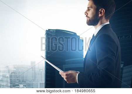 Side view of young businessman holding documet on sunlit city background. Work concept
