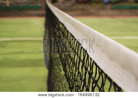 Tennis court net in warm sunlight. Tennis court divider. Opposite sites of competitors on tennis court. Summer day in tennis club. Outdoor sport and active lifestyle concept. Green field for game