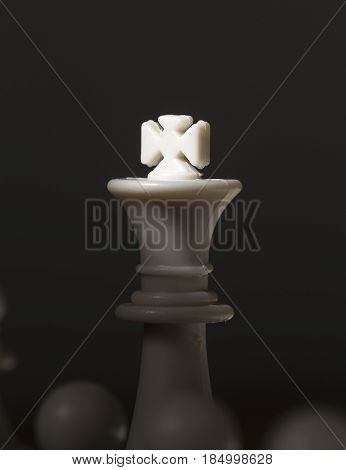 Chess figure king with light on crown. White chess king. Chessmate victory concept photo. White king between pawns. Chessboard game. Black and white vertical image of checkmate. Leadership metaphor