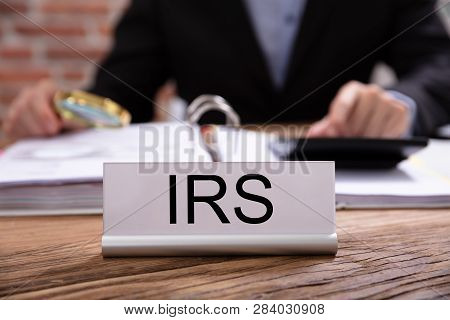 Nameplate With Irs Title Kept On Desk In Front Of Businessman Working In The Office