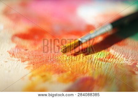 One Brush, Stained With Yellow Oil Paint, Lies On A Wooden Palette Lit By The Bright Sun