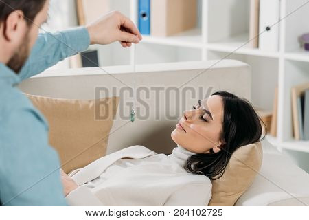 Cropped Shot Of Bearded Hypnotist Hypnotising Young Woman With Closed Eyes Lying On Couch