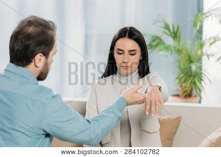 Bearded Hypnotist Holding Wrist Of Young Woman With Closed Eyes During Hypnotherapy