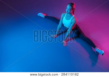 Attractive Young Slim Gymnast Woman In Sports Clothing Stretching On The Floor In Neon Lights. Flexi