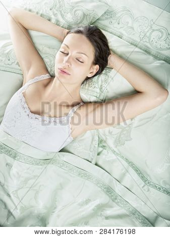 Beautiful young woman sleeping in luxury bed. Bed is made with linen embroidered percale.