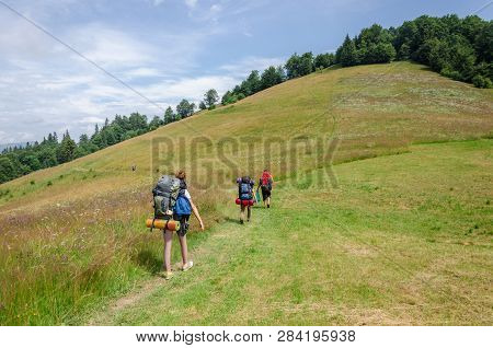 Several Tourists With Backpacks Go Along The Path In The Mountains. Horizontal Frame