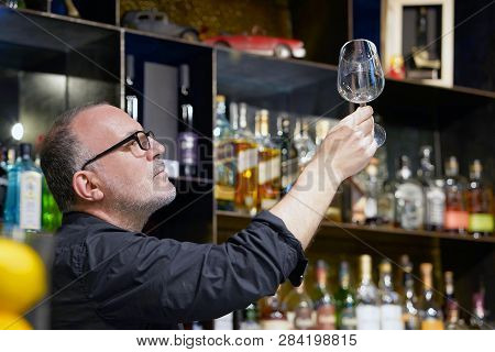 Elderly Bartender Cleans The Glass. A Handsome Bartender Polishes A Glass Of Wine Glasses. The Conce