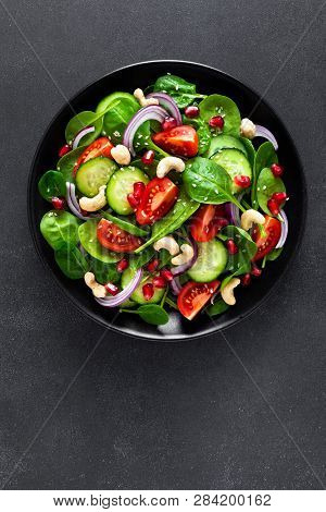 Spinach Salad With Fresh Cucumbers, Tomato, Onion, Pomegranate, Sesame Seeds And Cashew Nuts On Blac