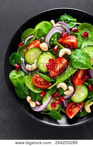 Spinach Salad With Fresh Cucumbers, Tomato, Onion, Pomegranate, Sesame Seeds And Cashew Nuts On Blac