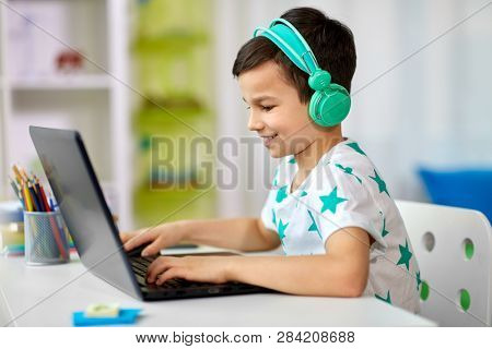 technology, gaming and people concept - boy in headphones playing video game on laptop computer at home