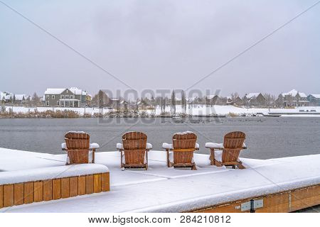 Snowy Deck With Chairs Overlooking Lake And Homes