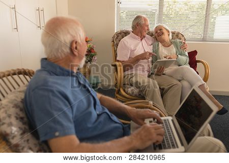 Side view of active senior man using laptop looking senior couple using digital tablet at nursing home