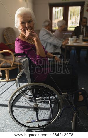 Side view of disable senior woman sitting on whee chair and looking at camera in home