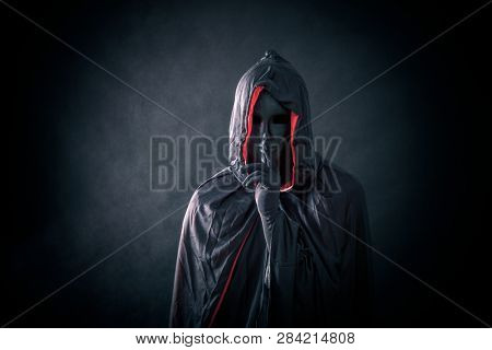 Scary figure with black mask in hooded cloak 