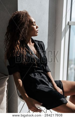 Portrait of stylish african american woman wearing housecoat sitting near window indoor