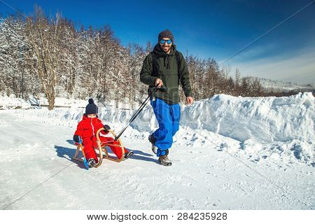Happy Father And His Son Enjoying Sledding Ride. Happy Family With Sled In Winter Having Fun Togethe