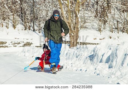 Happy Father And His Son Enjoying Sledding Ride. Happy Family With Sled In Winter Having Fun Togethe
