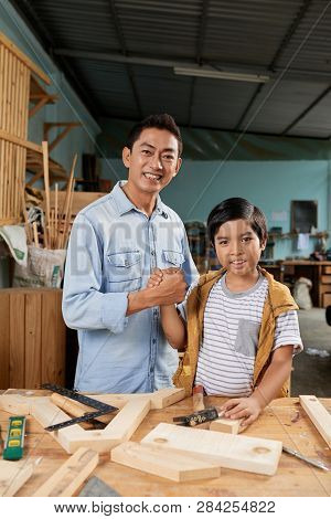 Pround Father And His Happy Son Shaking Hands After Working With Wood In Garage