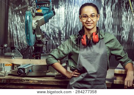Smiling Craftswoman Grinding Timbers With Special Machine. Beautiful Woman Wearing Safety Glasses. C