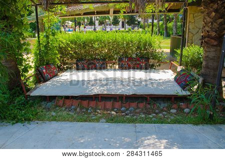 Bed On The Street With Colorful Pillows Near The Bushes