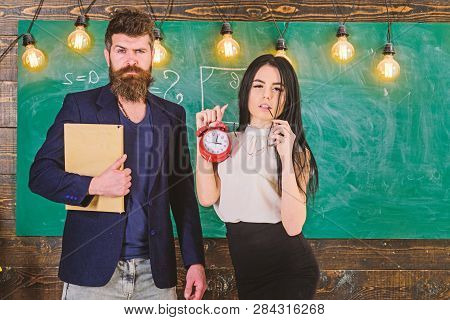 Man With Beard Hold Book And Sexy Girl Teacher Holds Alarm Clock, Chalkboard On Background. Lady Tea