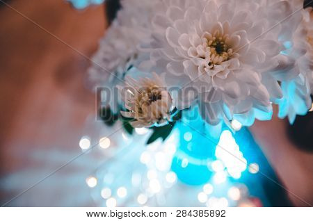 Lights Shining Behind The Bouquet Of White Fresh Flowers. Top View On The Decoreted Wooden Table.