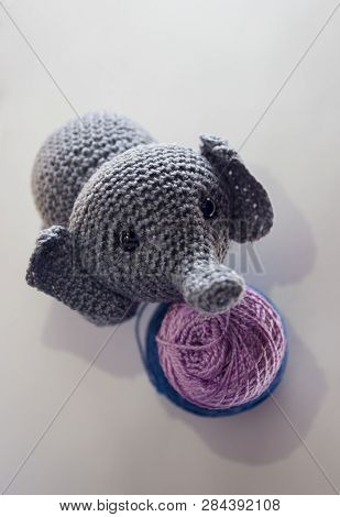 Little Grey Elephant Crocheted Standing Behind Lilac And Blue Tangles Of Thread On White Background