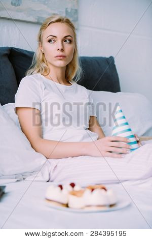 Uspet Woman Holding Party Hat While Celebrating Birthday In Bed Alone