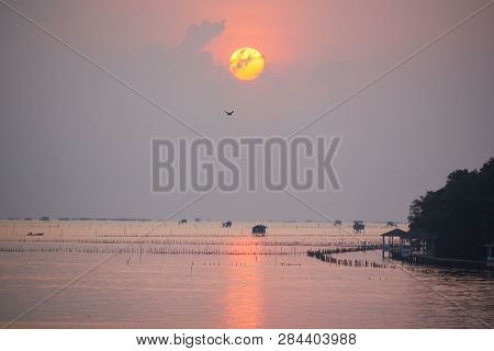 Scene Of Sunrise Over The Ocean And Flying Bird. Houses Of Fishermen And Boat Sialing In The Sea