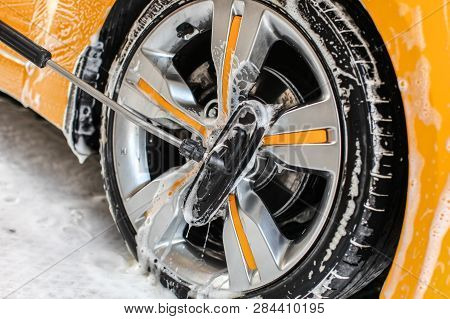 Yellow Car Wheel Washed In Self Service Carwash, Brush Cleaning Aluminium Rim Disc Covered In Shampo