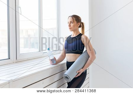 People, Sport And Fitness Concept - Young Woman With Yoga Mat And Bottle Of Water Standing Near Wind