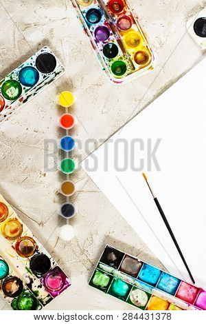 Flatlay With Bright Paints In Small Round Containers And Many Palettes, Brush And White Sheet Of Pap