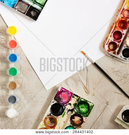 Flatlay With Bright Paints In Small Round Containers And Many Palettes, Brush And White Sheet Of Pap